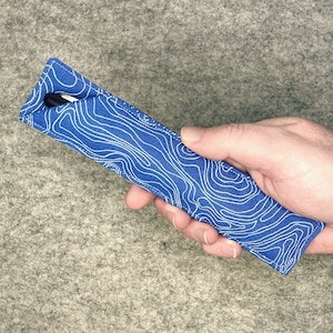 May include: A blue fabric pen case with a white topographic pattern. The case is being held in a hand.