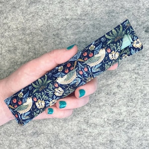 May include: A blue fabric pouch with a floral and bird pattern. The pouch is holding a light blue pen.