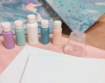 May include: A set of five small plastic squeeze bottles containing acrylic paint in lavender, mint green, white, teal, and peach, alongside two blank white canvases, two abstract pour-painted canvases, and a clear plastic cup.