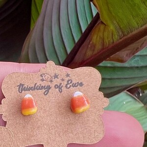Puede incluir: Pendientes de caramelo de maíz, cada uno con secciones amarillas, naranjas y blancas. Los pendientes están en una etiqueta marrón con el texto "Thinking of Ewe".