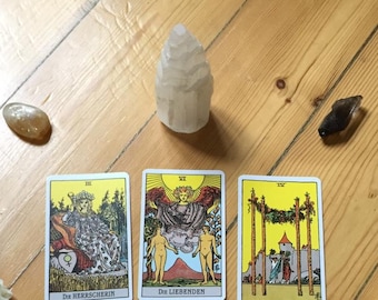 Può includere: Una stesa di tarocchi con tre carte verticali etichettate Die Herrscherin, Die Liebenden e IV, e un mazzo sormontato dalla carta Ritter der Kelche. Due rose bianche, una punta di cristallo e tre pietre levigate sono disposte attorno ad esse.