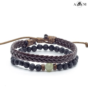 May include: Two bracelets, one brown leather braided bracelet with a black lava rock bead bracelet layered on top. The lava rock bracelet has a green stone bead and a wooden bead.