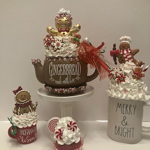 May include: A collection of festive gingerbread-themed decorations. Includes a brown teapot with "GINGERBREAD made with love" text, a red mug with "GINGERBREAD kisses" text, a white mug with "MERRY & BRIGHT" text, and a cupcake with peppermint candies.