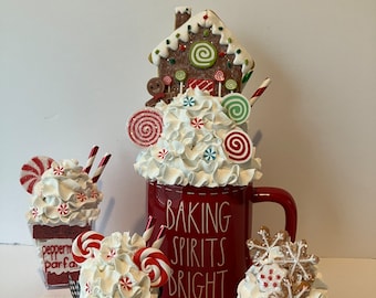 May include: A collection of faux holiday treats including a large red mug labeled BAKING SPIRITS BRIGHT topped with a gingerbread house, a small red mug labeled PEPPERMINT KISSES, a peppermint parfait cup, and a cupcake topped with snowflake cookies.
