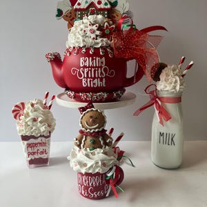 May include: A red teapot with the text Baking Spirits Bright, topped with faux whipped cream and a gingerbread house. Beside it, a peppermint parfait, a mug with a gingerbread figure and text Gingerbread Kisses, and a milk bottle with a red ribbon.