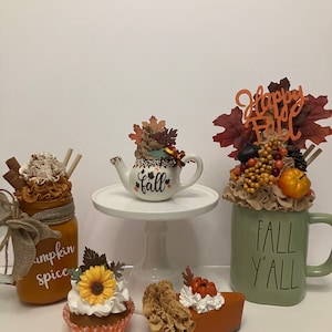 May include: Fall themed decorations including a pumpkin spice mason jar, a teapot with fall leaves, a mug with the text "Fall Y'all", a cupcake with a sunflower, and a slice of pumpkin pie.