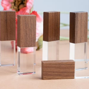 Op de afbeelding: Een verzameling rechthoekige blokken, elk bestaande uit een donkerbruin houten bovendeel bevestigd aan een heldere, transparante acrylbasis. Sommige blokken staan verticaal, terwijl één blok horizontaal op de voorgrond ligt.