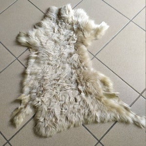 May include: A white sheepskin rug with a soft, fluffy texture. The rug is laid out on a tiled floor.
