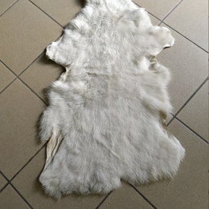 May include: A white sheepskin rug with a soft, fluffy texture. The rug is laid out flat on a tiled floor.
