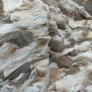 Puede incluir: Primer plano de una manta de piel suave, beige y gris. La piel está dispuesta en un patrón de patchwork, creando una textura suave y lujosa.