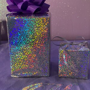 May include: Two iridescent gift boxes with a purple bow on top of the larger box. The boxes are on a purple surface with the word "Only" written in iridescent letters.