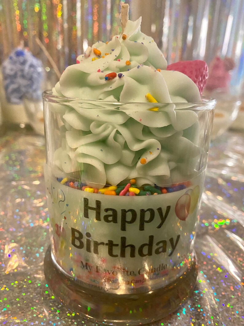 May include: A green cupcake candle in a clear glass jar with sprinkles and the words "Happy Birthday" on the label.