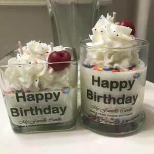 May include: Two glass jars with white frosting and sprinkles, topped with a red cherry. The jars have a black label that reads "Happy Birthday" and "My Favorite Candle".