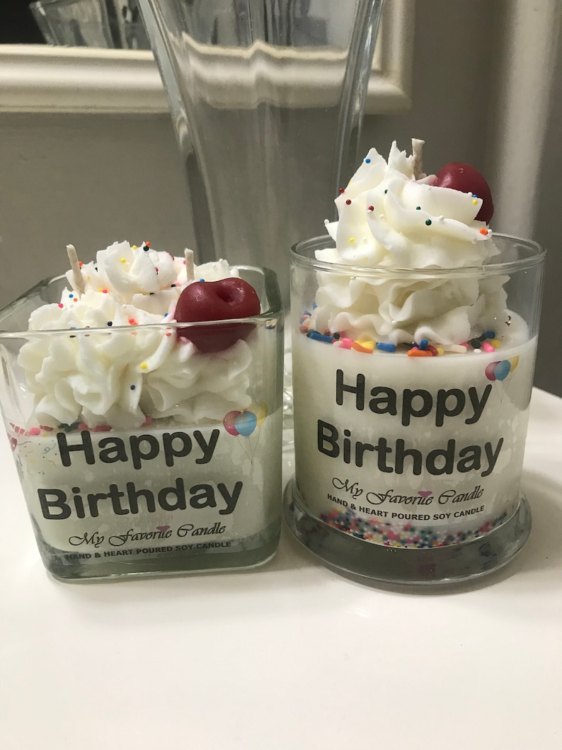 May include: Two glass jars with white frosting and sprinkles, topped with a red cherry. The jars have a black label that reads "Happy Birthday" and "My Favorite Candle".