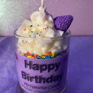 May include: A purple candle in a glass jar with a white frosting design and colorful sprinkles. The candle has a purple strawberry on top and says "Happy Birthday My Favorite Candle" on the label.
