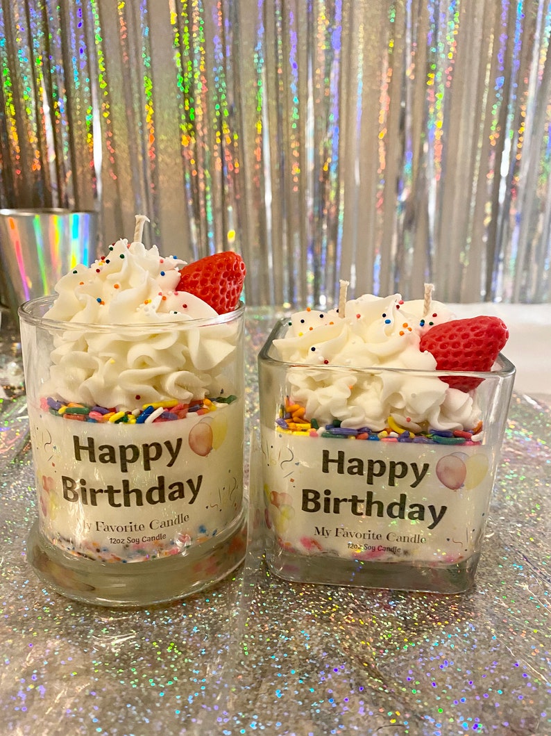 May include: Two square glass jars with white frosting, colorful sprinkles, and a red strawberry on top. The jars are labeled "Happy Birthday" and "My Favorite Candle" with a 12oz soy candle description.