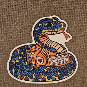 May include: A colorful sticker featuring a cartoon snake with blue scales, an orange backpack, and a red tongue. The backpack has the text "EMOTIONAL SURPORT". The snake is decorated with hearts.