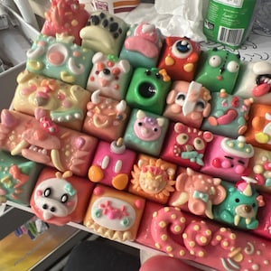 May include: A collection of colorful, hand-painted keycaps featuring various cartoon characters and designs. The keycaps are arranged in a grid pattern and are made of a smooth, glossy material.