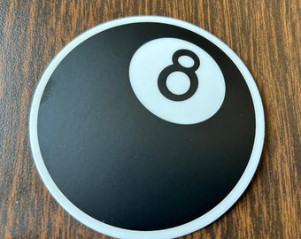May include: A black and white 8-ball sticker with a white outline. The 8-ball is a classic symbol of billiards and pool.
