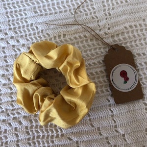 May include: A yellow satin scrunchie with a brown tag that has a white circle with two red roses and a green stem.