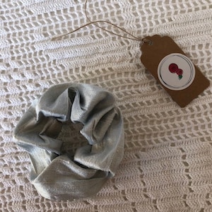 May include: A light blue satin scrunchie hair tie. The scrunchie is on a white crocheted surface.