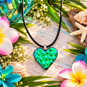 May include: A heart-shaped pendant made of vibrant green glass with a textured, scale-like pattern. The pendant is attached to a simple black cord necklace, featuring a silver-toned metal bail connecting the glass heart to the cord.