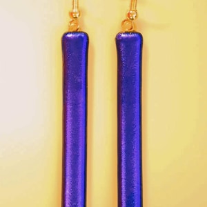 May include: A pair of dangle earrings featuring elongated, rectangular pendants in a vibrant, iridescent blue-purple hue. The earrings have gold-colored hooks and connectors, creating a striking contrast against the colorful pendants.