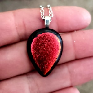 May include: A red and orange glass pendant with a black metal bail and chain. The pendant is teardrop shaped and has a textured surface.