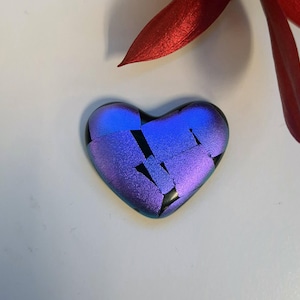 May include: A dichroic glass heart pendant with a vibrant blue and purple color shift. The heart is composed of multiple glass pieces, creating a mosaic effect. A red petal is in the background.