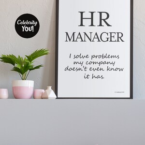 Pu&ograve; includere: Una stampa incorniciata in bianco e nero con la scritta "HR MANAGER" e una citazione umoristica. Una piccola pianta in vaso e oggetti decorativi sono su una mensola sottostante. Un adesivo circolare in bianco e nero con la scritta "Celebrity You!" &egrave; sul muro.