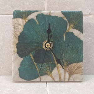 Può includere: Orologio quadrato con un design a foglie verdi e dorate. L'orologio ha lancette nere e un centro dorato.