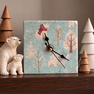 May include: A square wall clock with a light blue marble-like background featuring illustrations of polar bears in scarves and stylized trees. The clock has black hour, minute, and second hands centered on the face, creating a winter-themed design.