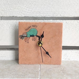 May include: A pink marble clock with a sloth wearing a turquoise shirt and the text "PYJAMA PARTY".