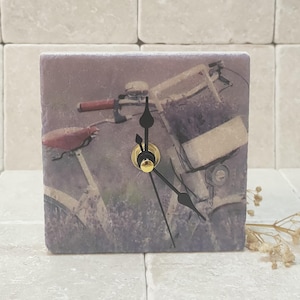 May include: A square clock with a vintage bicycle image on a slate background. The clock has black hands and a gold centre.