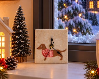 May include: A square stone clock featuring a brown dachshund illustration wearing a red and white patterned sweater. The clock has a beige, textured surface with black hour, minute, and second hands centered on the face of the dog graphic.