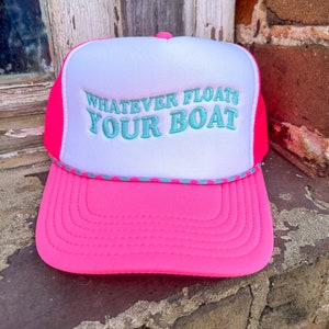 May include: Pink and white trucker hat with a turquoise embroidered saying "Whatever Floats Your Boat"