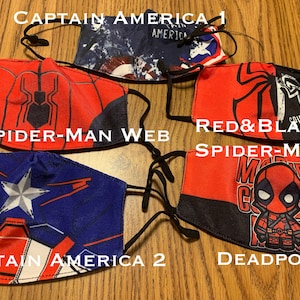 May include: Five different face masks with various superhero themes. The masks are red, blue, and black with images of Captain America, Spider-Man, and Deadpool. The text on the masks reads "Captain America 1", "Spider-Man Web", "Red & Black Spider-Man", "Captain America 2", and "Deadpool".