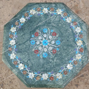 May include: Green marble octagonal table with floral inlay. The table features a central floral design and a border of white, blue, and red flowers. The table's dimensions are approximately 30 inches in diameter.