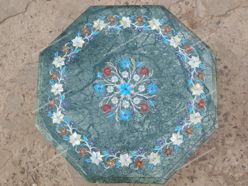 May include: Green marble octagonal table with floral inlay. The table features a central floral design and a border of white, blue, and red flowers. The table's dimensions are approximately 30 inches in diameter.