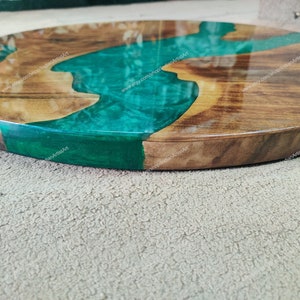 May include: A round wooden serving tray with a green epoxy resin river design. The tray has a natural wood finish and a smooth, polished surface.