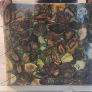 Pu&ograve; includere: Una piastrella quadrata in agata, con un mosaico di fette di agata marrone, verde e giallo. La piastrella ha una superficie lucida ed &egrave; adatta per l'uso come piano da tavolo o decorazione murale.