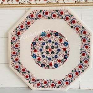 Puede incluir: Mesa octogonal de mármol blanco con intrincadas incrustaciones florales. La mesa presenta un diseño circular central y un borde de flores rojas, azules y verdes. La mesa tiene aproximadamente 76 cm de diámetro.