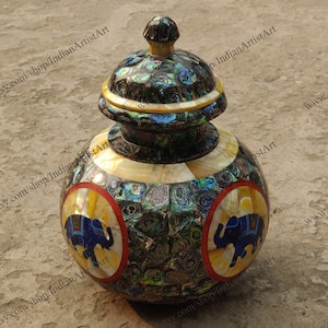 May include: A round, black, and iridescent decorative jar with a lid. The jar is decorated with two elephants in circles. The jar is made of inlaid mother of pearl.