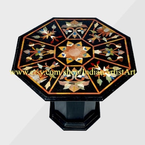 Pode incluir: Mesa octogonal de mármore preto com um design de incrustação geométrico apresentando motivos florais em várias cores, incluindo vermelho, amarelo, azul e verde. A mesa tem uma base de mármore preto.