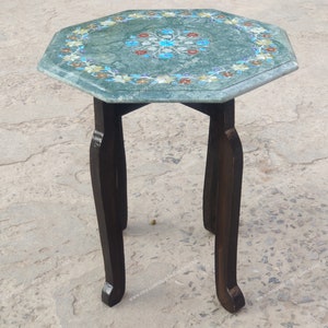 May include: A small, octagonal side table with a green marble top inlaid with floral patterns in shades of blue, red, and yellow. The dark brown wooden legs are curved. The table is approximately 20 inches tall.