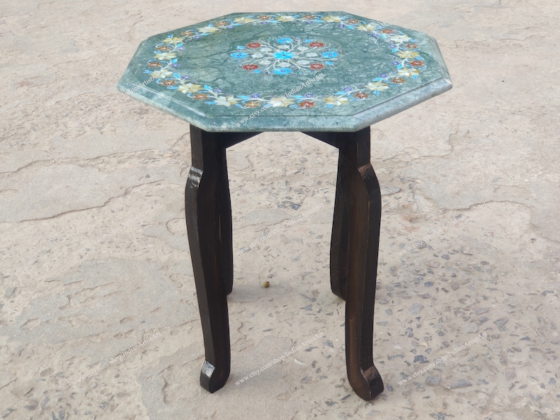 May include: A small, octagonal side table with a green marble top inlaid with floral patterns in shades of blue, red, and yellow. The dark brown wooden legs are curved. The table is approximately 20 inches tall.