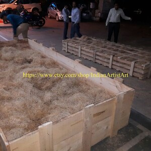 May include: A large wooden crate filled with brown packing material. The crate is sitting on a concrete surface. The text "https://www.etsy.com/shop/IndianArtistArt" is visible on the crate.