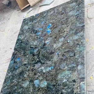 Può includere: Primo piano di una lastra di labradorite blu lucidata. La pietra ha uno sfondo blu scuro con macchie iridescenti blu e verdi.