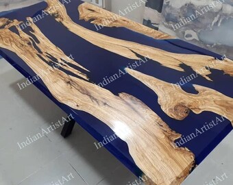 Pode incluir: Um tampo de mesa de madeira com um derrame de resina epóxi azul. A resina tem um design fluido, semelhante a um rio. A madeira é de cor castanho claro com um padrão de grão natural. O tampo da mesa é retangular e tem um acabamento liso e polido.