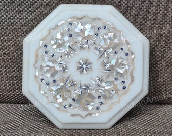 May include: White marble octagonal table top with inlaid floral design. The intricate pattern features mother-of-pearl and blue accents. A decorative piece for home decor, the table top is a unique and elegant addition.